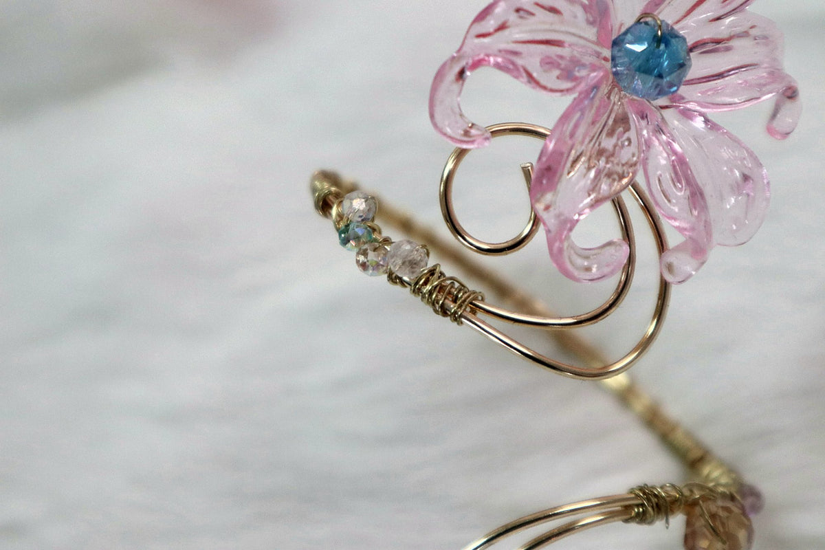 Close-up of a gold-coloured wire arm cuff with a pink flower and blue bead