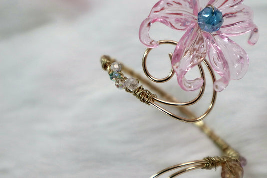 Close-up of a gold-coloured wire arm cuff with a pink flower and blue bead